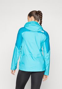 Letvægts hættejakke i gradient nuancer af blå med en tekstureret overflade. Har logoet på ryggen og lange ærmer.