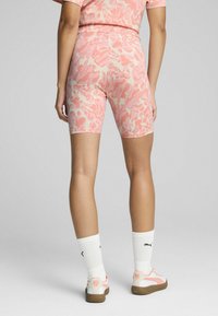 Pink and cream patterned bike shorts with a high waist. Model wearing white socks and pink-accented sneakers. Smooth fabric texture.
