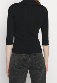 Top nero a coste con colletto, dotato di maniche a tre quarti e un design aderente. Abbinato a jeans scuri a vita alta.