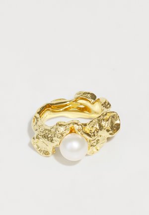 Auksinis žiedas su tekstūruotu, abstrakčiu dizainu ir centriniu baltu perlu. Juostos forma nelygi ir skulptūriška, suteikianti vizualinį gilumą.