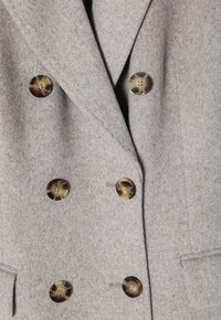 Abrigo gris de doble faz, confeccionado en un tejido suave, con grandes botones marrones estampados y bolsillos laterales. Superficie texturizada visible.