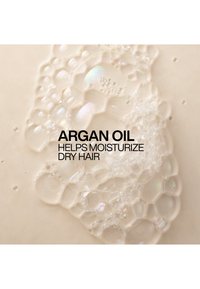 Des bulles claires sur une surface beige avec un texte noir indiquant que l'huile d'argan aide à hydrater les cheveux secs.