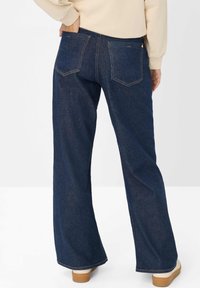 Donkerblauwe denim flared jeans met een middelhoge taille, zichtbare stikdetails en twee achterzakken. Eenvoudig ontwerp, geen versieringen.