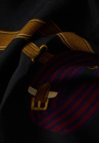 Tekstil med sort baggrund og gyldne accenter, indviklede mønstre i lilla og rød samt et markant grafisk element, der ligner en spænde.