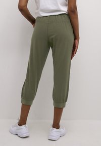 Kort olivgröna byxor med elastisk midja och uppvikta fållar, tillverkade av ett lätt tyg. Matchas med vita sportskor.