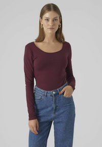 Haut bordeaux à manches longues avec un décolleté arrondi, associé à un jean bleu taille haute, présentant une texture en denim classique et des détails de poches.