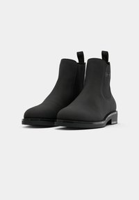 Botas Chelsea negras con acabado liso y mate y paneles laterales elásticos. Cuenta con una suela de goma plana y tiradores para facilitar su uso.