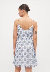 Rochie albă cu model floral albastru, bretele subțiri, corset ajustat și fustă evazată. Material ușor cu textură netedă.