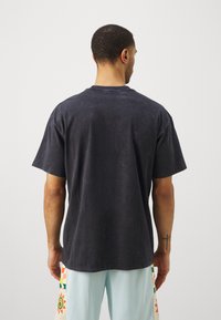 Camiseta negra de manga corta con un ajuste relajado y una superficie ligeramente texturizada, vista desde atrás. Diseño simple, sin adornos.