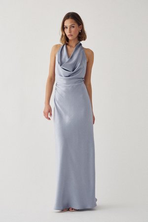 Femeie care poartă o rochie fără mâneci, din satin argintiu, până în podea, cu un decolteu tip glugă drapat, stând în fața unui fundal simplu, de culoare deschisă.