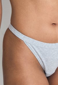 Sivý bavlnený tanga s tenkým elastickým pásom. Tkanina je melírovaná a hladká, predstavujúca jednoduchý, minimalistický dizajn.