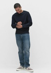 Granatowy sweter z okrągłym dekoltem; niebieskie dżinsy; szaro-białe sneakersy. Ubranie charakteryzuje się luźnym krojem i miękkimi materiałami.