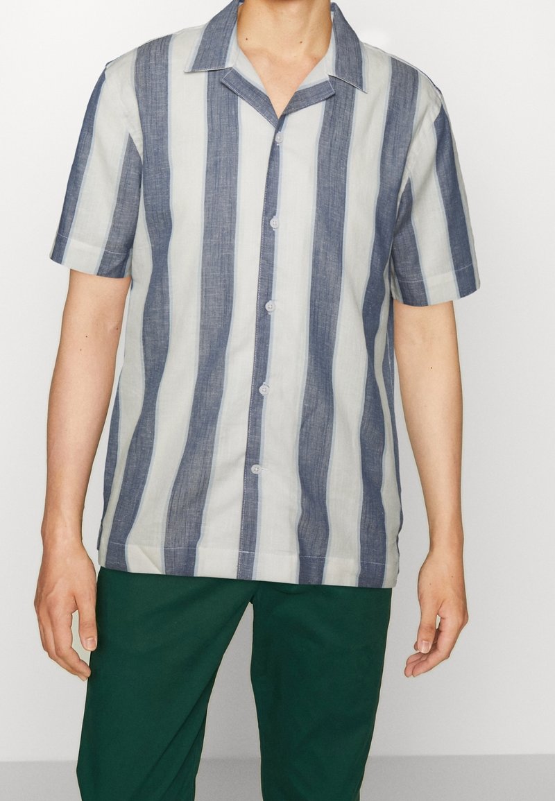 Chemise à manches courtes boutonnée avec des rayures verticales bleues et blanches, dotée d'un col, d'une texture subtile et d'une coupe décontractée. Les boutons sont visibles.