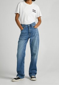 White cotton t-shirt with "Pepe Jeans" logo, paired with light blue high-waisted jeans and black low-top sneakers with white soles.
