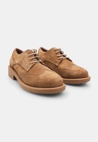 Scarpe in suede con lacci di colore marrone chiaro, punta rotonda, dettagli cuciti e tacco in legno solido. Caratterizzate da una superficie liscia e un design classico.
