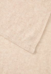 Tecido bege claro, textura suave, mostrando duas camadas sobrepostas. Uma borda apresenta um acabamento limpo, tricotado, com ligeiros detalhes de nervura.