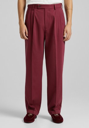 Pantaloni plissettati bordeaux con vita alta, realizzati in un tessuto liscio. Presentano una chiusura con un bottone e tasche laterali. Vestibilità sartoriale.