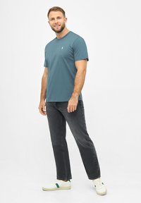 Teal katoenen t-shirt met ronde hals, gecombineerd met zwarte jeans en witte sneakers met groene accenten. Eenvoudig, effen ontwerp.