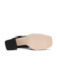 Chaussure à talon carré noire avec une tige en cuir lisse et une semelle beige. La semelle est dotée d'un talon en caoutchouc noir texturé pour l'adhérence.