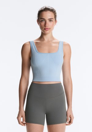 Woman wearing a light blue ribbed crop top and high-waisted dark gray fitted shorts, standing against a plain white background.