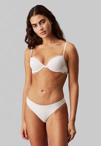 Reggiseno imbottito bianco con spalline regolabili e slip bikini a vita bassa coordinato. Tessuto liscio e setoso con dettagli di cuciture minime.
