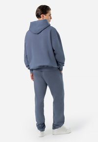 Hooded sweatshirt and matching pants in soft, light blue fabric. Relaxed fit with ribbed cuffs; worn with white sneakers.