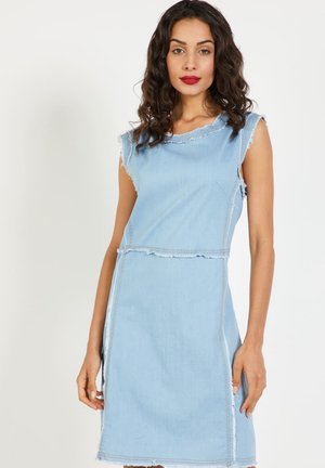 Vestido de mezclilla azul claro con dobladillo deshilachado, diseño sin mangas y escote en forma curva. La tela tiene una textura suave con costuras visibles.