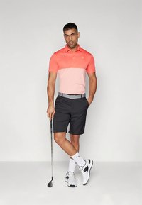 Pánsky golfový outfit pozostávajúci z dvojfarebnej polokošele v ružovej a koralovej, čiernych šortiek a bielych golfových topánok s čiernymi detailmi.