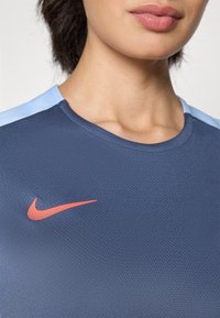 Navy blue athletic shirt with textured fabric, crew neck, and light blue accents on the shoulders. Features a red Nike logo.