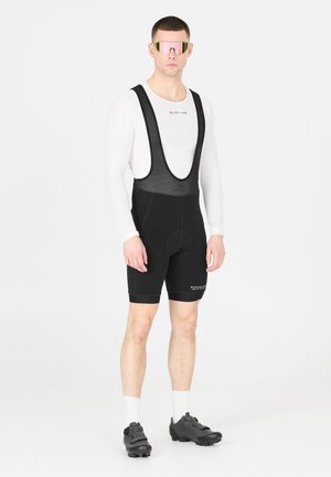 Pantaloni bib da ciclismo da uomo, neri con spalline in rete, con fondello imbottito. Maglia a maniche lunghe bianca come base, occhiali da sole specchiati rosa, scarpe da ciclismo nere.