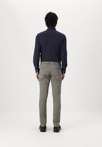 Navy-blauwe longsliv shirt met knoopmanchetten, gecombineerd met lichtgrijze tailorpants en zwarte schoenen, gezien van achteren tegen een witte achtergrond.