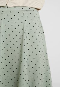 Lichtgroene rok gemaakt van zachte stof, met zwarte stippen, plooien en een gladde textuur. Geen zichtbare accessoires of accenten.