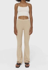 Beige geribbelde high-waisted broeken gecombineerd met een witte geribbelde crop top. De broeken hebben een uitlopende onderkant en de outfit heeft dunne bandjes.