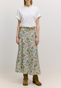 Weißes T-Shirt mit hochgeschlagenen Ärmeln, kombiniert mit einem floralen Maxereich mit Pastellfarben und einem braunen Wildleder-Stiefeletten mit Schnallen-Detail.
