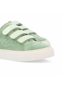 Baskets en suede vert avec trois bandes Velcro brillantes au motif reptilien et une semelle en caoutchouc texturée blanche ; détail de design perforé sur les côtés.