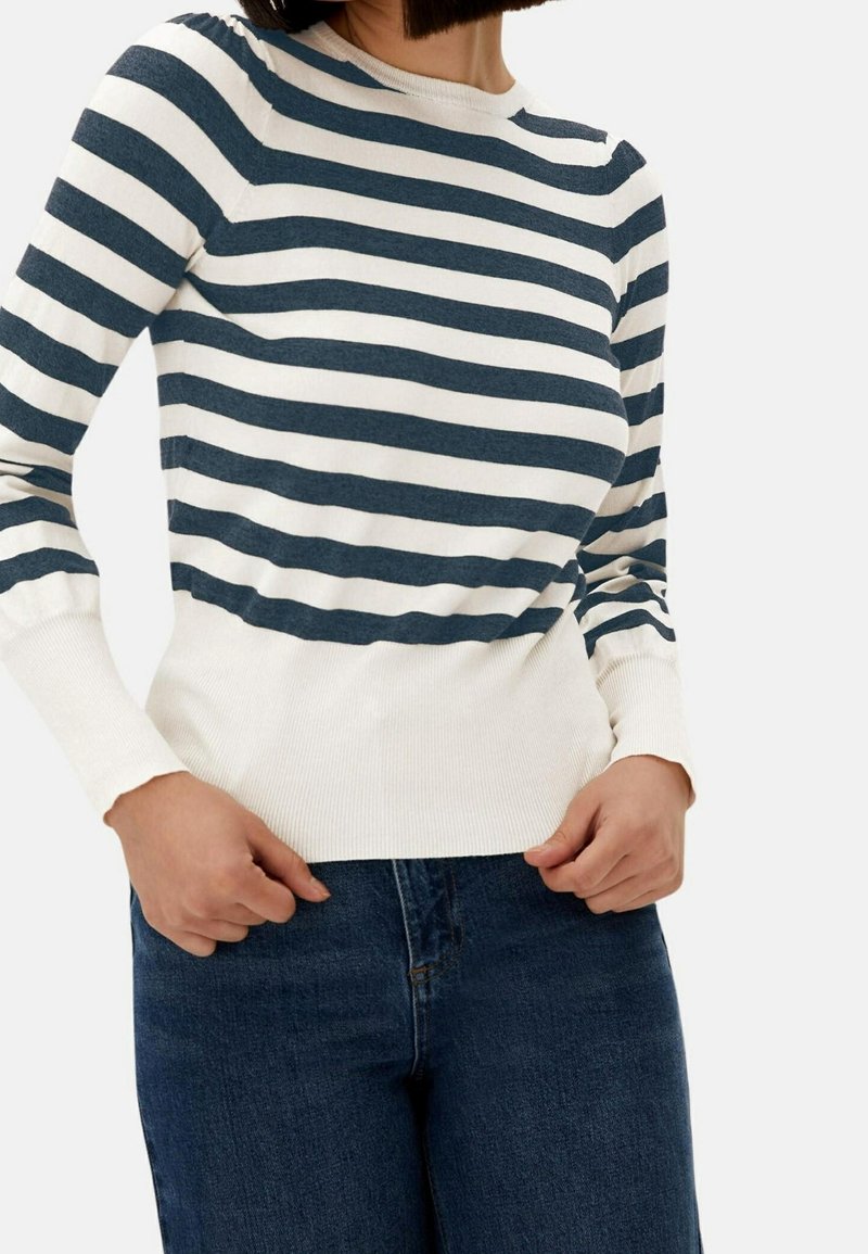 Maglione a righe blu navy e bianco a maniche lunghe con texture a coste e collo rotondo. Abbinato a jeans in denim blu scuro.