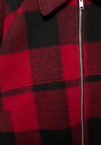 Czerwona i czarna kurtka w kratę wykonana z mieszanki wełny, z zamkiem błyskawicznym i szpiczastym kołnierzem. Teksturowana powierzchnia z różnorodnością wzoru.