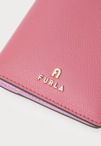 Furla novčanik od teksturirane ružičaste kože s zlatnim logotipom i istaknutim šavovima. Kompaktni dizajn s zaobljenim rubovima i glatkim unutarnjim podstavljanjem.