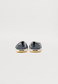 Marineblå flip-flops med en teksturert såle og kontrastfarge i gult på yttersålen. Har et enkelt design og en bakre logolabel.