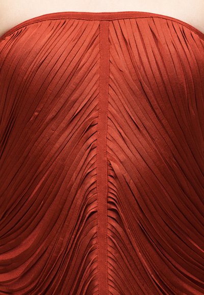 Κοντινό πλάνο σκούρου πορτοκαλί πτυχωτού υφάσματος με κάθετη ραφή στο κέντρο.
