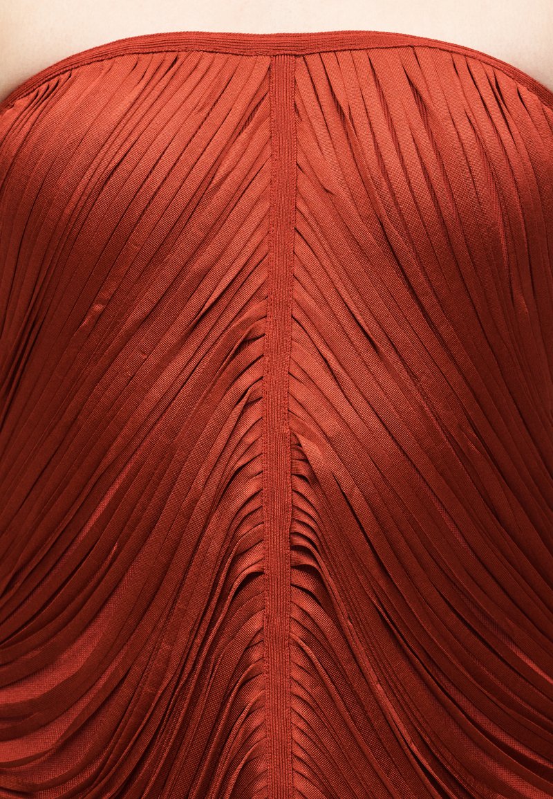 Gros plan sur un tissu plissé orange foncé avec une couture verticale au centre.