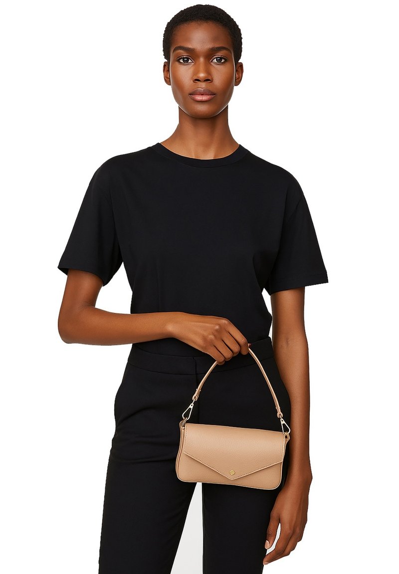 Borsa in pelle color tabacco con una forma strutturata, caratterizzata da una patta pieghevole e un manico corto. Il modello indossa una t-shirt nera e pantaloni.