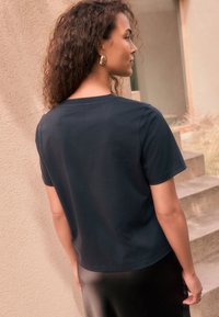 Marineblauw katoenen t-shirt met korte mouwen, ronde hals en een losse pasvorm, gecombineerd met een zwarte satijnen rok. Minimalistisch ontwerp.