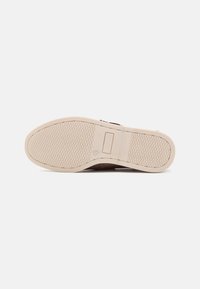 Suela de zapato con una superficie de goma texturizada y de color beige. Presenta un logo rectangular incrustado cerca del área del talón.