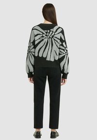 Maglione lavorato a maglia con un motivo floreale grigio su sfondo nero. Caratterizzato da maniche lunghe, scollatura rotonda e polsini a coste. Abbinato a pantaloni neri.
