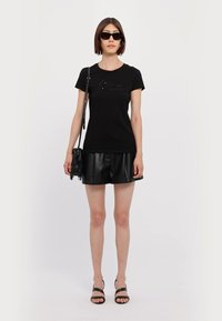 T-shirt in cotone nero con design aderente, abbinato a una mini gonna in pelle nera. Gli accessori includono occhiali da sole scuri e una piccola borsa con frange.