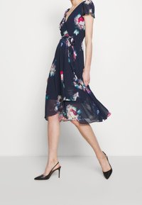 Laivastonsininen kukkakuosisekoitettu mekko lyhyillä puffihihoilla, vyötäröltä kiristetty ja halkaisijaltaan kauniisti valuva helma. Yhdistetty mustiin avokkaisiin, joissa on sanka.