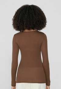 Braunfarbener Langarmshirt aus weichem, dehnbarem Material. Verfügt über einen Rundhalsausschnitt und eine körpernahe Passform, mit minimalen Nähten und ohne sichtbare Beschläge.