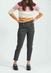 Pull rayé multicolore en rose, bordeaux et orange. Jean noir fuselé avec poches latérales. Mocassins noirs brillants avec accents dorés.