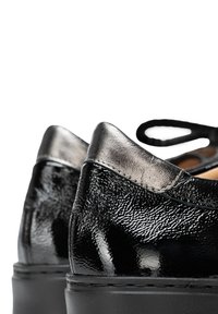 Scarpe in pelle sintetica nera lucida con una finitura testurizzata, caratterizzate da un accento in metallo argento sul tacco e una forma arrotondata. Progettate con chiusura a lacci.